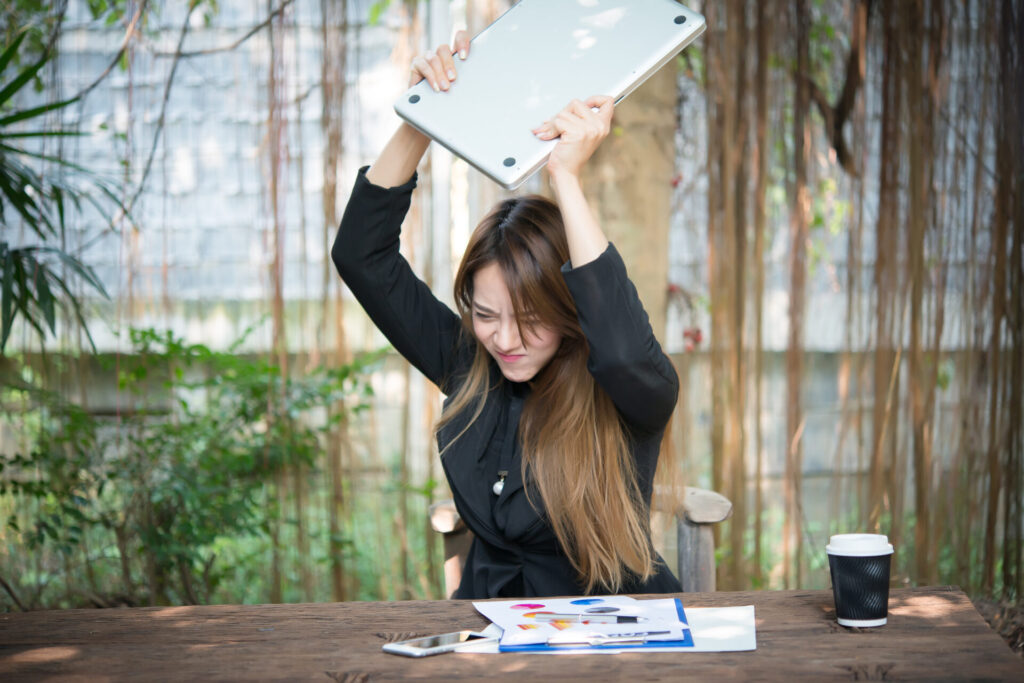 屋外のカフェでノートパソコンを振り上げて怒る女性