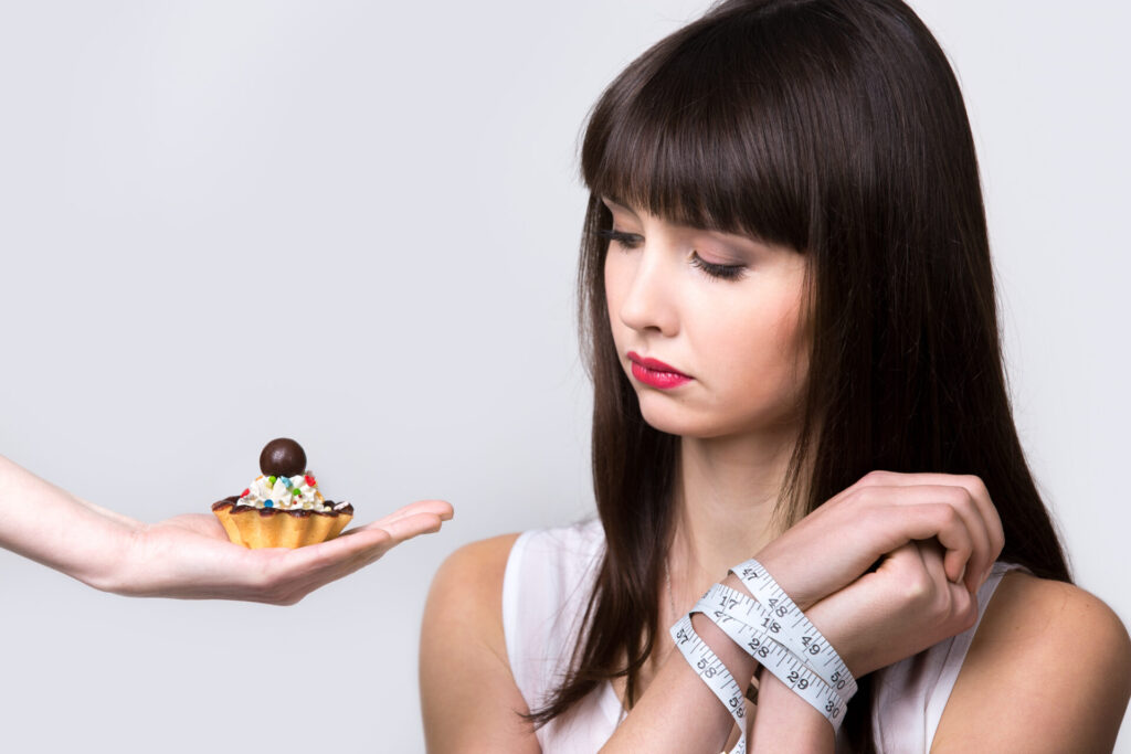 ケーキを見つめながら手をメジャーで縛られている女性
