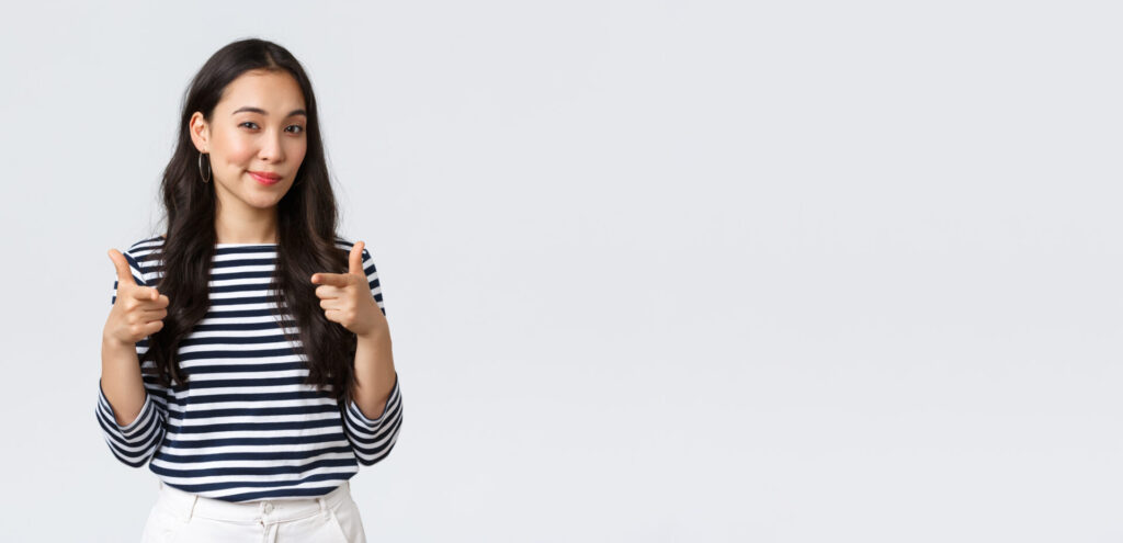 ボーダーシャツを着た女性が指差しポーズをして微笑んでいる様子