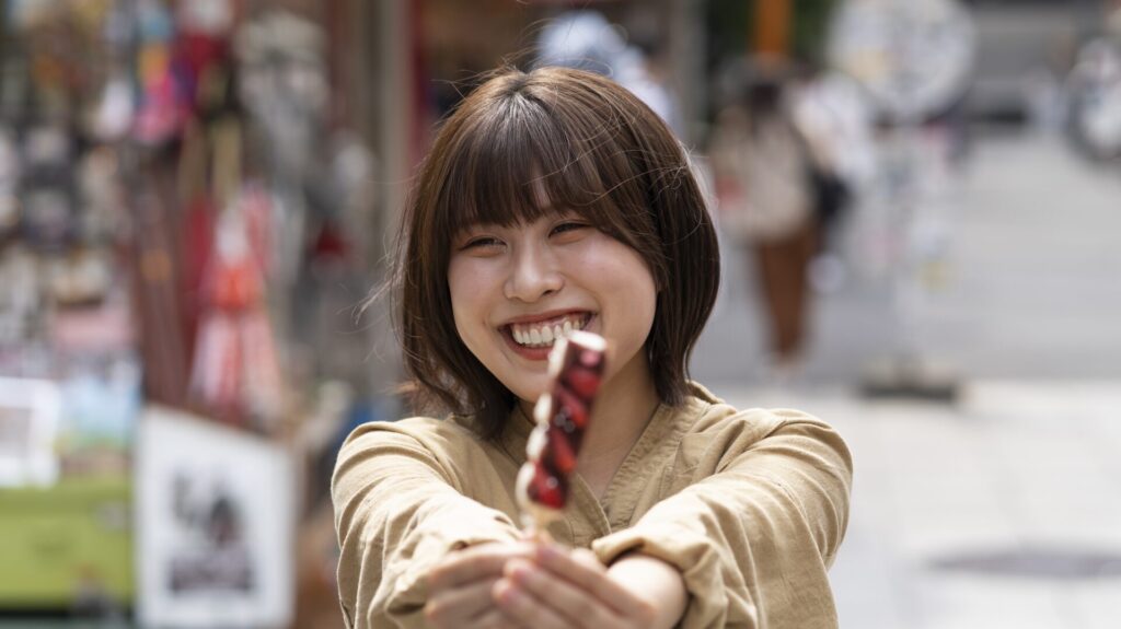 「ふしぎ駄菓子屋銭天堂」の駄菓子を手に持って、嬉しそうに微笑んでいる若い女性