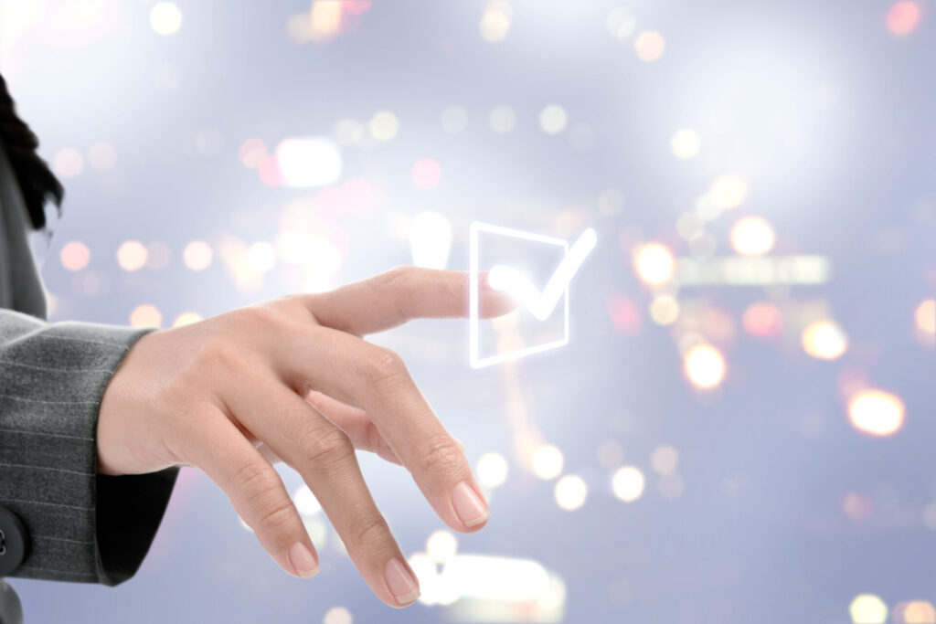 空中のチェックマークに指を伸ばす女性の手元イメージ
