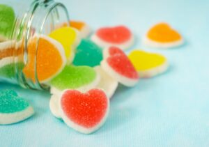 ガラス瓶からこぼれ出す、カラフルなハート型で砂糖がまぶされたグミ。「キュン グミ」の甘酸っぱいイメージ。